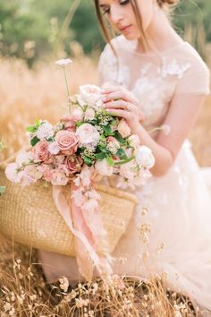 a woman kneeling down holding a basket filled with flowers