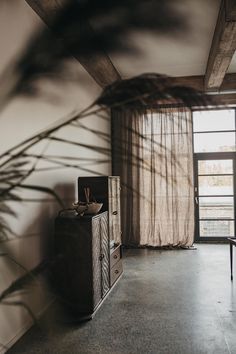 a living room with a large window and a dresser next to a plant in the corner