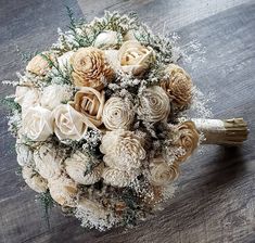 a bridal bouquet with white flowers and pine cones on a wooden table, ready to be used as a bride's bouquet