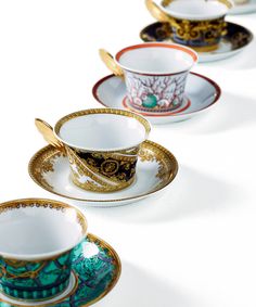 five tea cups and saucers lined up on a white table top with gold trimmings