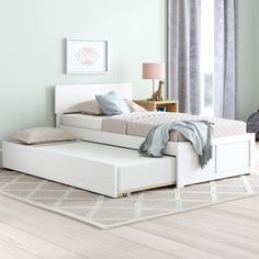 a white bed sitting on top of a hard wood floor next to a window with curtains