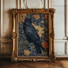 a black bird sitting on top of a wooden floor in front of a framed painting