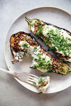 a white plate topped with two stuffed eggplant halves covered in cheese and herbs