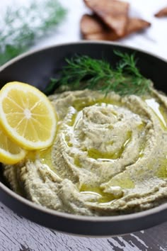 a black bowl filled with hummus and lemon wedges