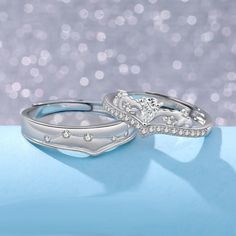 two wedding rings sitting on top of a blue surface with sparkles in the background