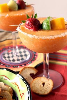 two glasses filled with fruit sitting on top of a table next to crackers and bread