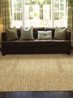 a brown couch sitting in front of a window next to two pillows on top of a wooden floor