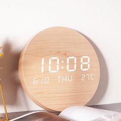 a wooden clock sitting on top of a table next to a vase with flowers and an open book