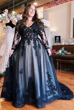 a woman in a black and grey dress standing on a wooden floor with dresses behind her