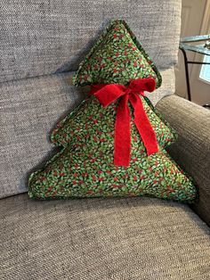 a christmas tree pillow sitting on the back of a couch with a red ribbon tied around it