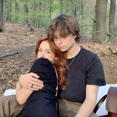 a man and woman sitting on a bench in the woods with their arms around each other