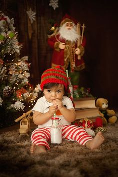 a baby sitting on the floor in front of a christmas tree wearing a santa clause hat