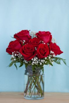 a vase filled with red roses and baby's breath in front of a blue background