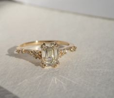 an engagement ring with a green emerald surrounded by small white and yellow diamonds on a sheet of paper