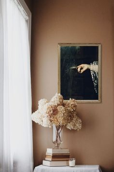 a vase filled with flowers sitting on top of a white table next to a painting