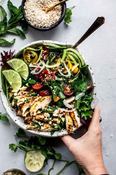 a person holding a bowl filled with chicken and veggies next to some rice