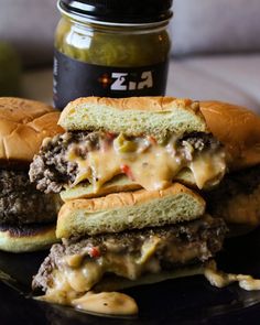 two cheeseburgers stacked on top of each other with pickles and sauce in the background