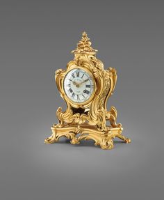 an ornate gold clock with roman numerals on the front and sides, sitting against a gray background