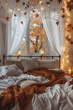 an unmade bed in front of a window with fall leaves hanging from the ceiling