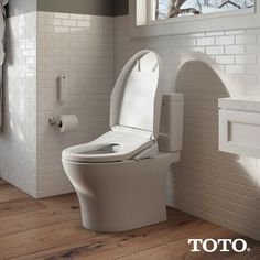 a toilet with the lid open in a white tiled bathroom, next to a roll of toilet paper