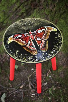 a butterfly painted on the side of a table with red legs and an orange top