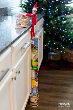 Take Elf on the Shelf to new heights. Elf on the Shelf Standing on Cans. Your Scout Elf can go anywhere by standing on cans. In this Elf idea, Elf got into the Kitchen Christmas cookies jar. New Elf on the Shelf ideas daily plus free Elf on the Shelf printables. #FrugalCouponLiving #ElfontheShelf #ElfontheShelfIdeas #ElfIdeas #funnyelfideas #funnyelfontheshelf #elfprintables #freeelfprintables #printables #freeprintables #ElfonaShelf #cans #cannedgoods #elfontheshelfhacks #elftricks #elftips Rock Climbing Elf On The Shelf, Elf Rock Climbing, Elf On The Shelf Gummy Bears, Easy Elf On The Shelf Ideas Kitchen, Elf On The Shelf Climbing, Diy Elf On The Shelf Ideas, Elf On The Shelf Diy, Elves Ideas, Elf On The Shelf Printables