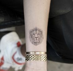 a small lion tattoo on the wrist is shown in black and grey ink with gold chains