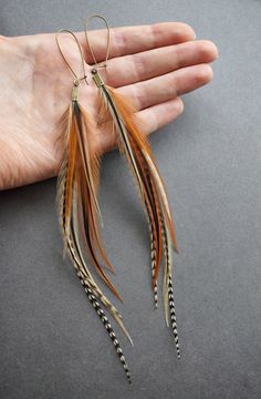 a pair of feather earrings is held in someone's hand on a gray surface