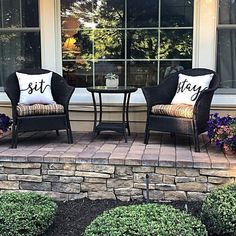 two chairs and a table with pillows on them sitting in front of a window that says sit stay