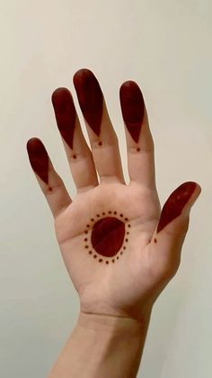 a person's hand with red nail polish on it and a circle design painted on the palm