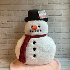 a snowman sitting on top of a pink blanket next to a white brick wall