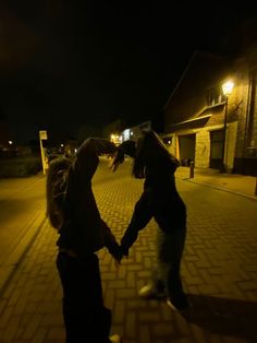 two people holding hands on a brick road at night with street lights in the background