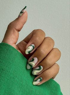 a woman's hand with green and white manicures holding onto a green sweater