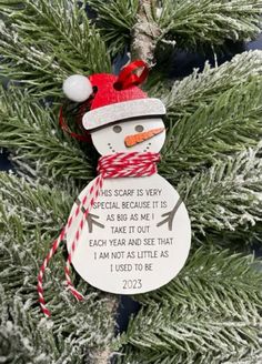 a snowman ornament hanging from a tree with a red and white ribbon