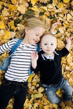 two young children laying on the ground covered in leaves and looking up at the camera