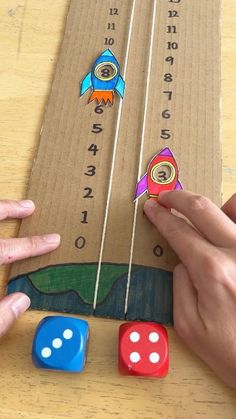 two hands are playing with some dices on a board that is made out of cardboard