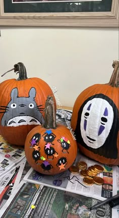 three pumpkins with faces painted on them sitting next to each other in front of a newspaper