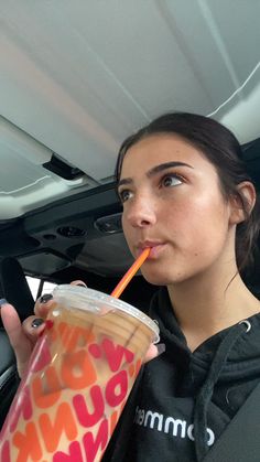 a woman holding a drink in her right hand and looking up at the camera with an orange straw in her other hand