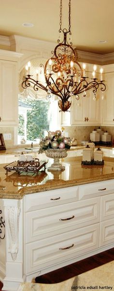 a chandelier hanging from the ceiling over a kitchen island with marble counter tops