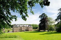 a large house sitting in the middle of a lush green field with trees around it