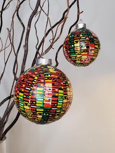 two christmas ornaments hanging from a tree branch with no leaves on it and one is multicolored