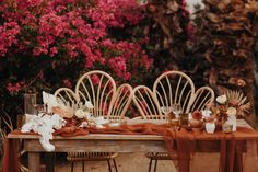 a wooden table topped with lots of white and orange flowers next to chairs covered in brown cloths