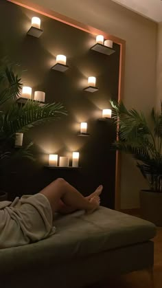 a woman laying on top of a couch in front of a wall with lights above it