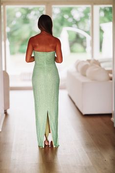 a woman in a green dress walking into a room with white furniture and large windows