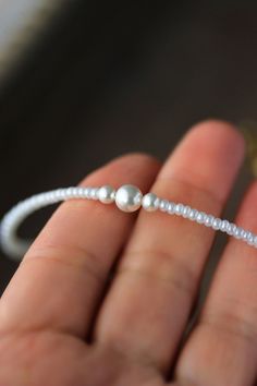 a close up of a person's hand holding a beaded bracelet with pearls