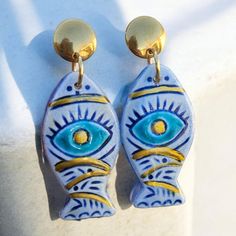 Enhance your jewelry collection with our unique Dangle Fish-Shaped Evil Eye Earrings. These striking earrings feature a handmade ceramic charm, intricately shaped like a fish and adorned with the iconic evil eye design. Each charm is crafted with care, ensuring that no two pieces are exactly alike, adding to their unique charm and character. The earrings are designed with a sturdy stainless steel stud, providing both durability and a sleek, modern look. Stainless steel is known for its hypoallergenic properties, making these earrings a great choice for those with sensitive ears. The fish-shaped evil eye charm is more than just a stylish accessory; it also carries a powerful symbolism of protection and good fortune. The dangle design adds a playful and elegant touch, making these earrings p Earrings Ceramic, Fish Earrings, Evil Eye Design, Earring Dangle, Evil Eye Earrings, Ceramic Earring, Fish Shapes, Eye Earrings, Evil Eye Charm