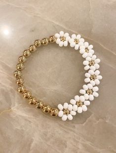 the white and gold beaded bracelet is set on top of a marble countertop