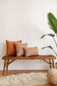 a wooden bench with two pillows and a potted plant in the corner next to it