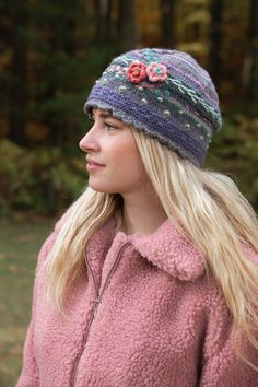 a woman wearing a pink jacket and a knitted hat with flowers on the side