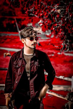 a young man wearing sunglasses standing in front of a red tree with leaves on it